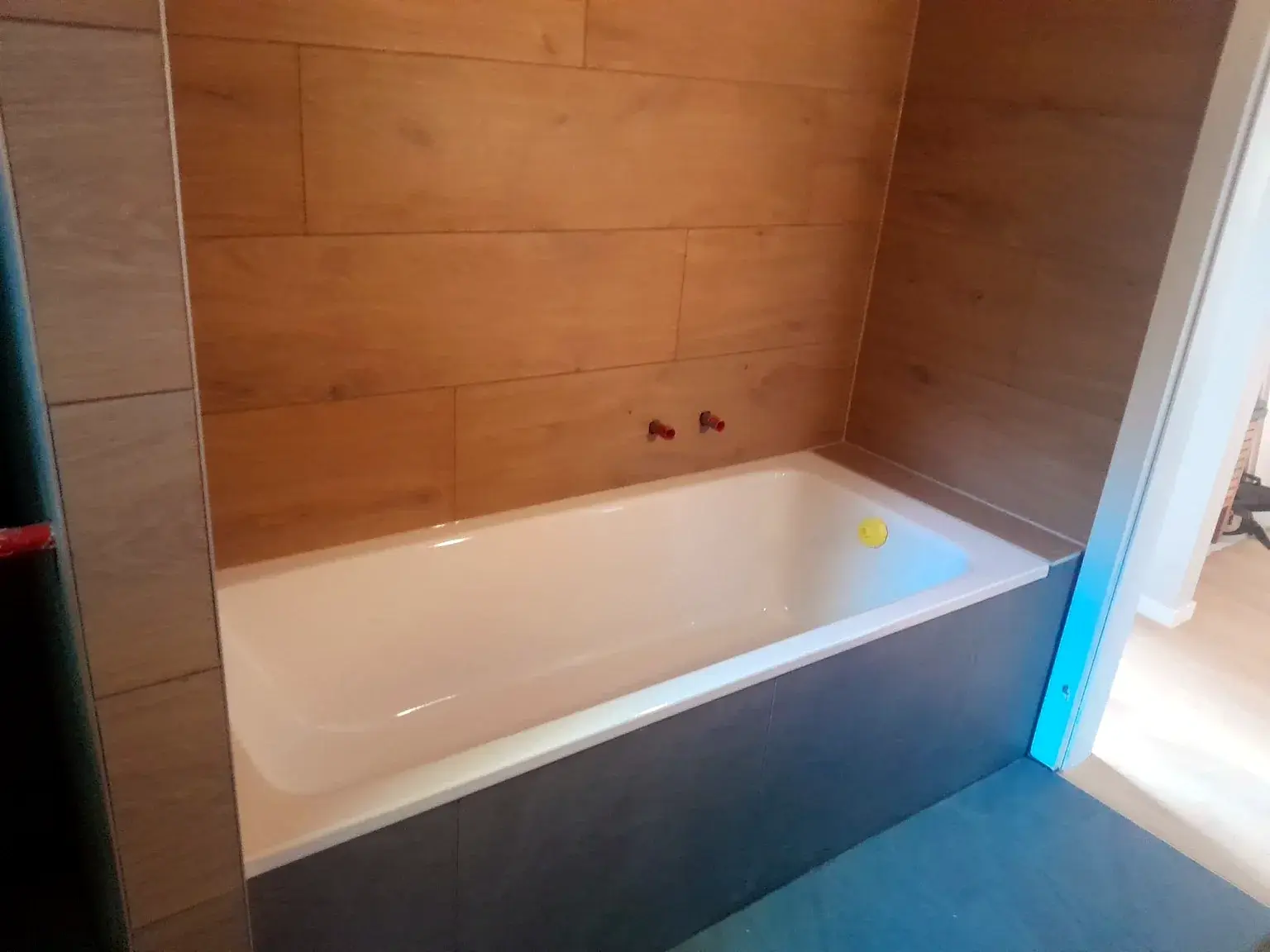 Baignoire encastrée avec habillage gris et revêtement mural effet bois.