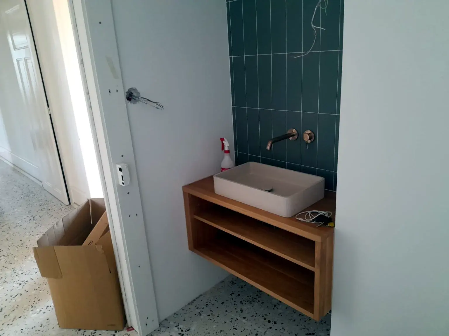 Meuble vasque suspendu en bois avec robinetterie murale sur carrelage vert.