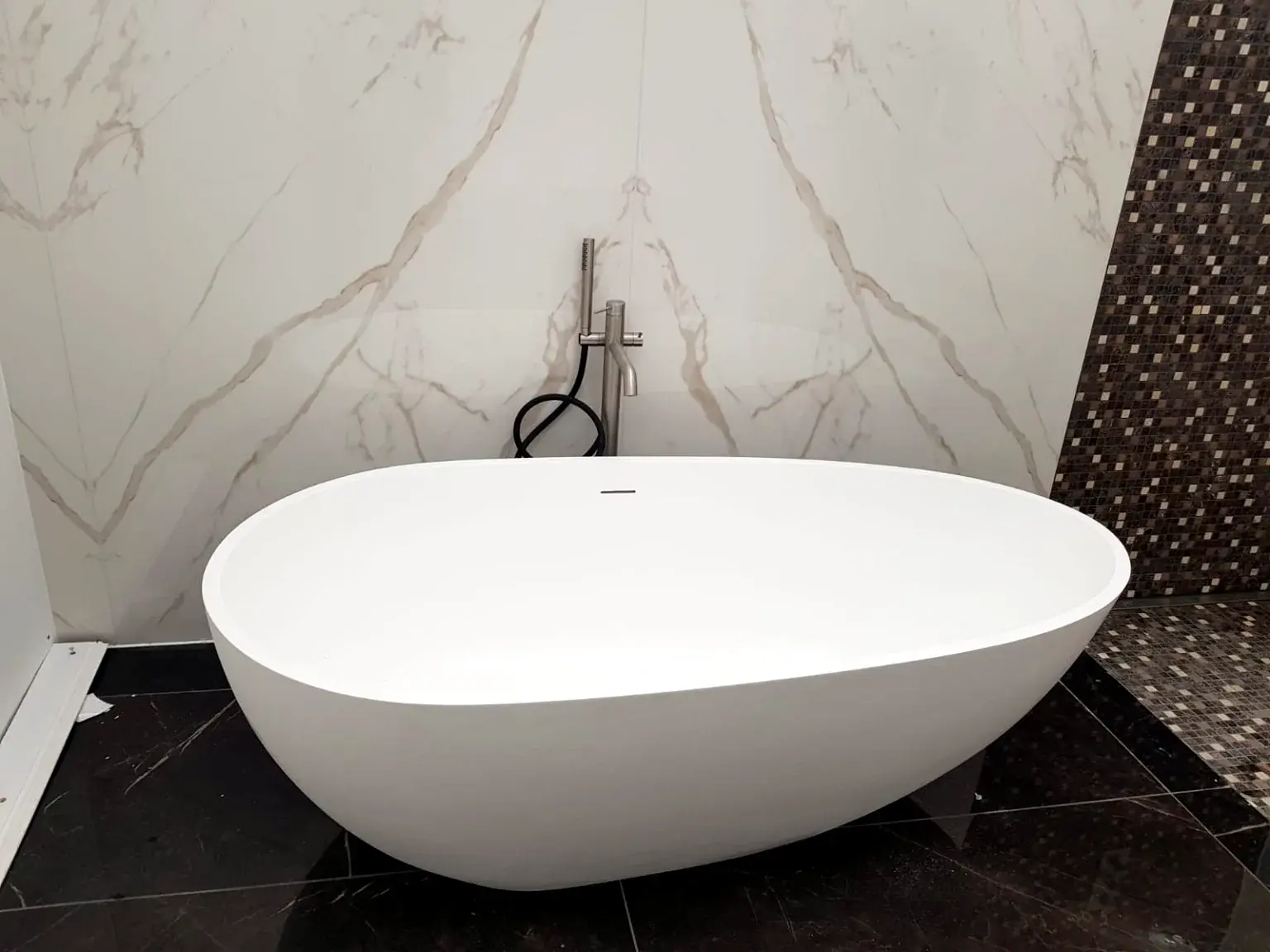 Baignoire îlot devant un revêtement mural effet marbre.