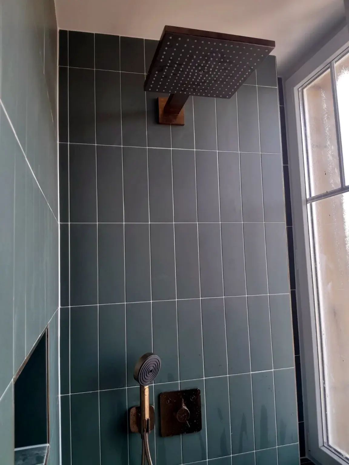 Détail de douche avec carrelage vert et robinetterie finition métal.