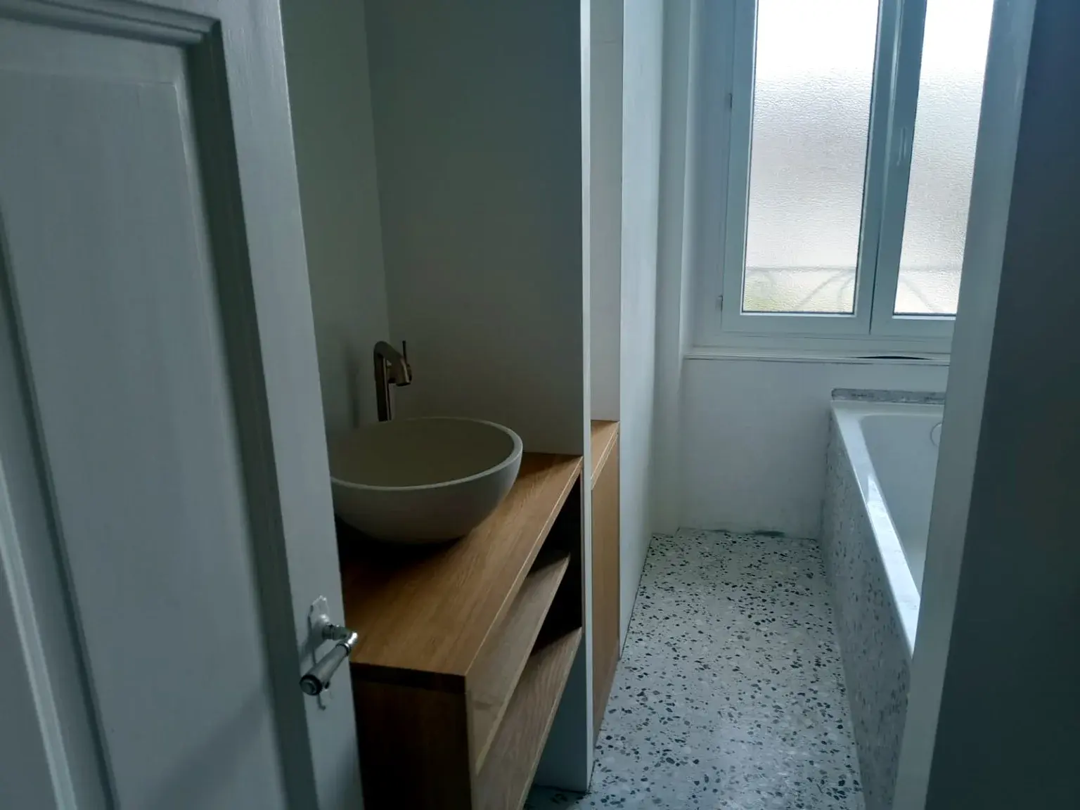 Salle de bains avec baignoire, meuble vasque bois et sol terrazzo.