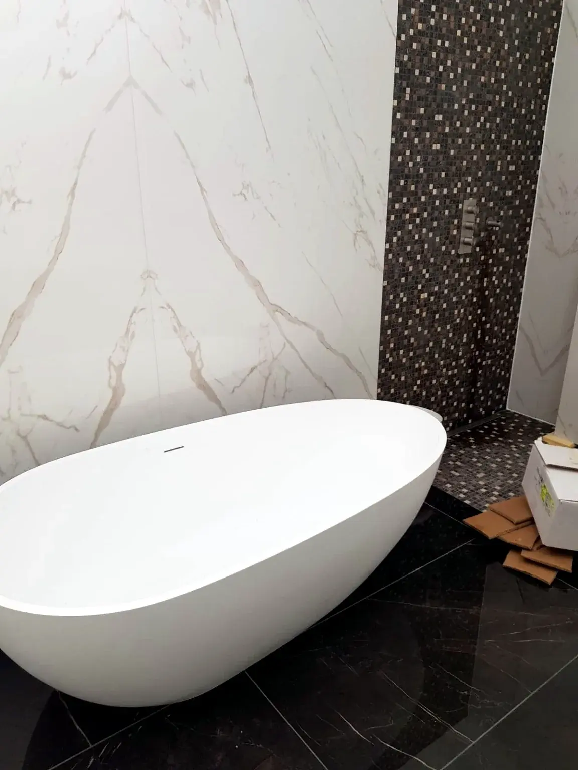 Baignoire îlot avec mur effet marbre et zone de douche en mosaïque sombre.