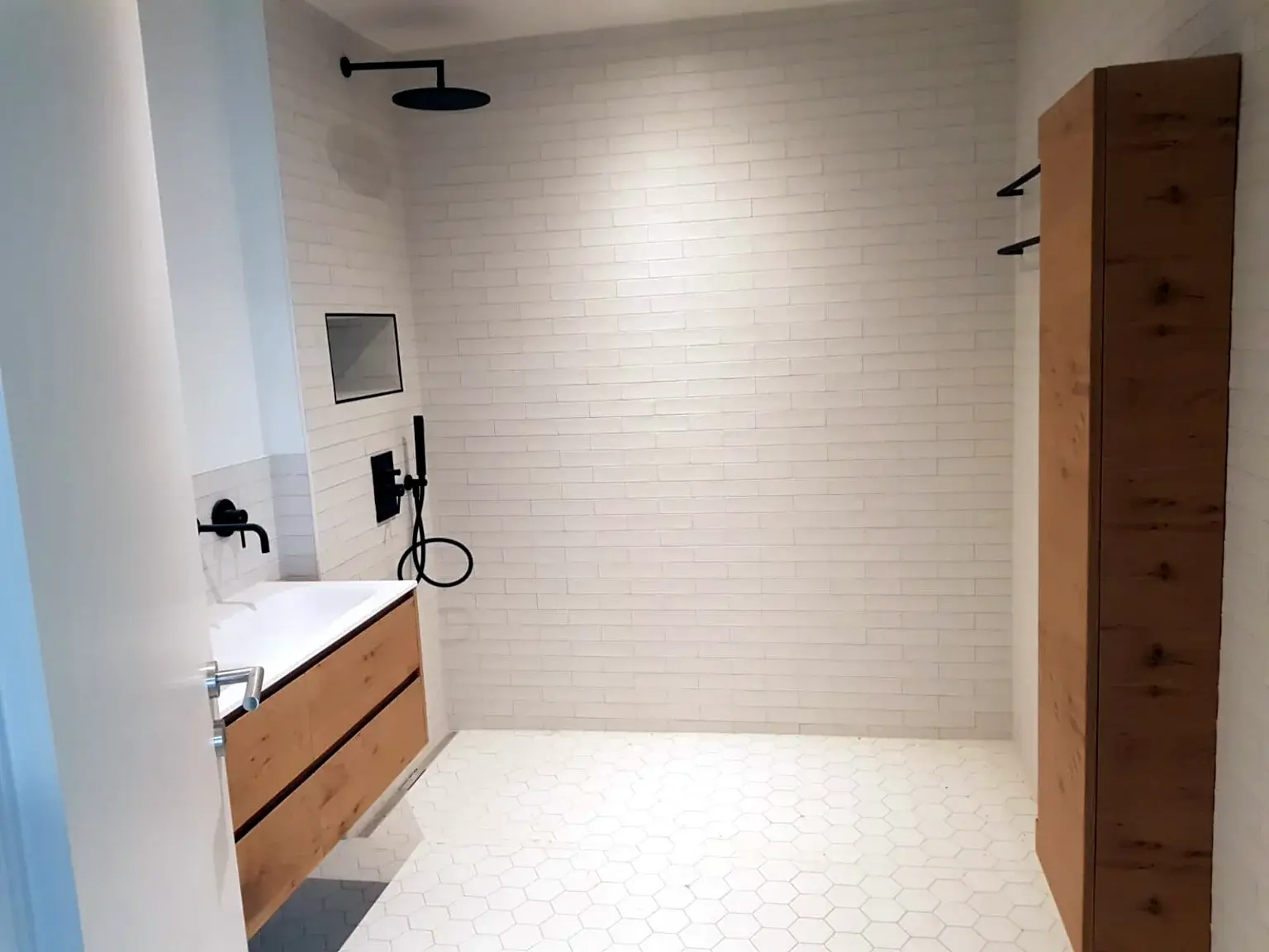 Salle de bains blanche avec grande douche à l’italienne et mobilier bois.