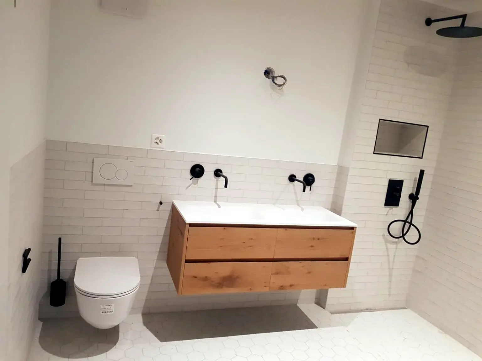 Salle de bains lumineuse avec meuble vasque bois, douche ouverte et sanitaires suspendus.
