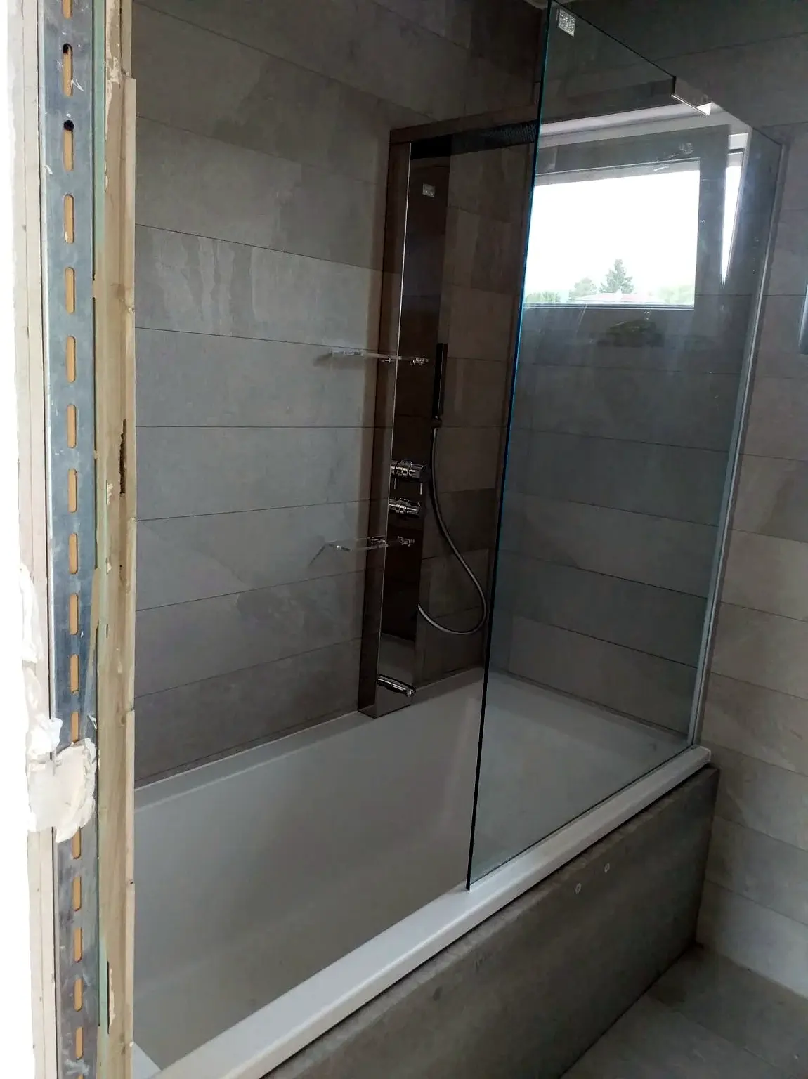 Baignoire équipée d’une paroi vitrée et d’une colonne de douche intégrée.