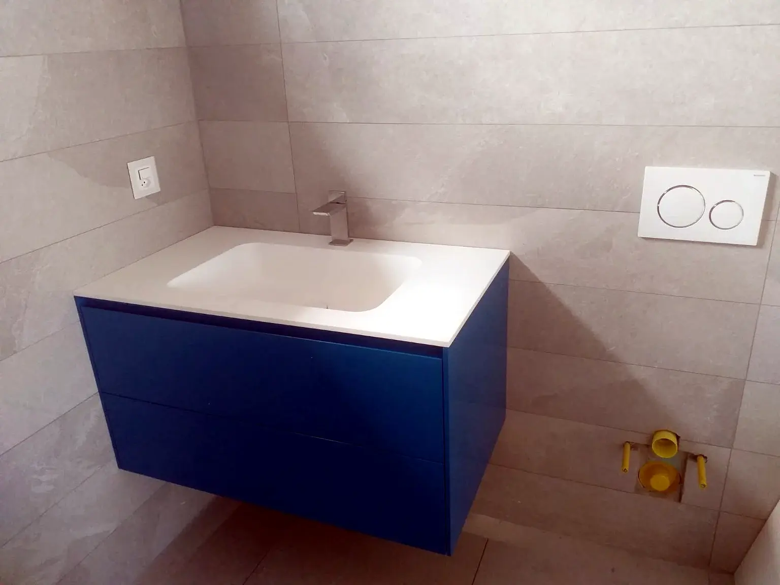 Meuble vasque suspendu bleu dans une salle de bains aux carreaux gris.