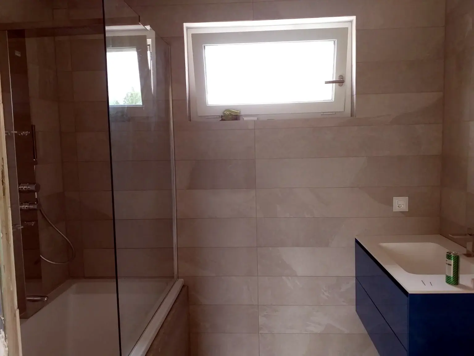 Salle de bains grise avec douche vitrée et meuble vasque bleu suspendu.