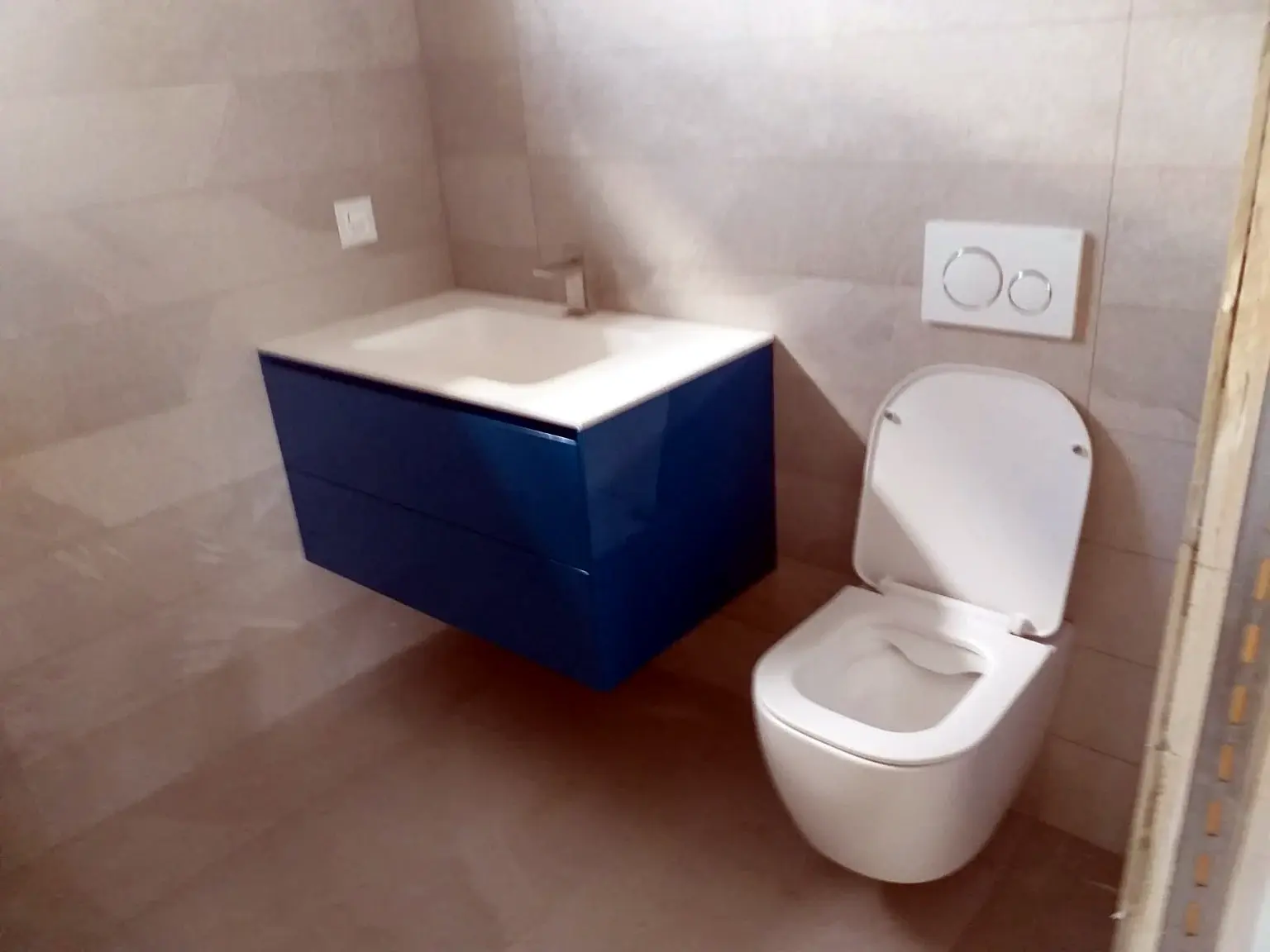 Salle de bains grise avec meuble vasque bleu suspendu et toilettes murales.
