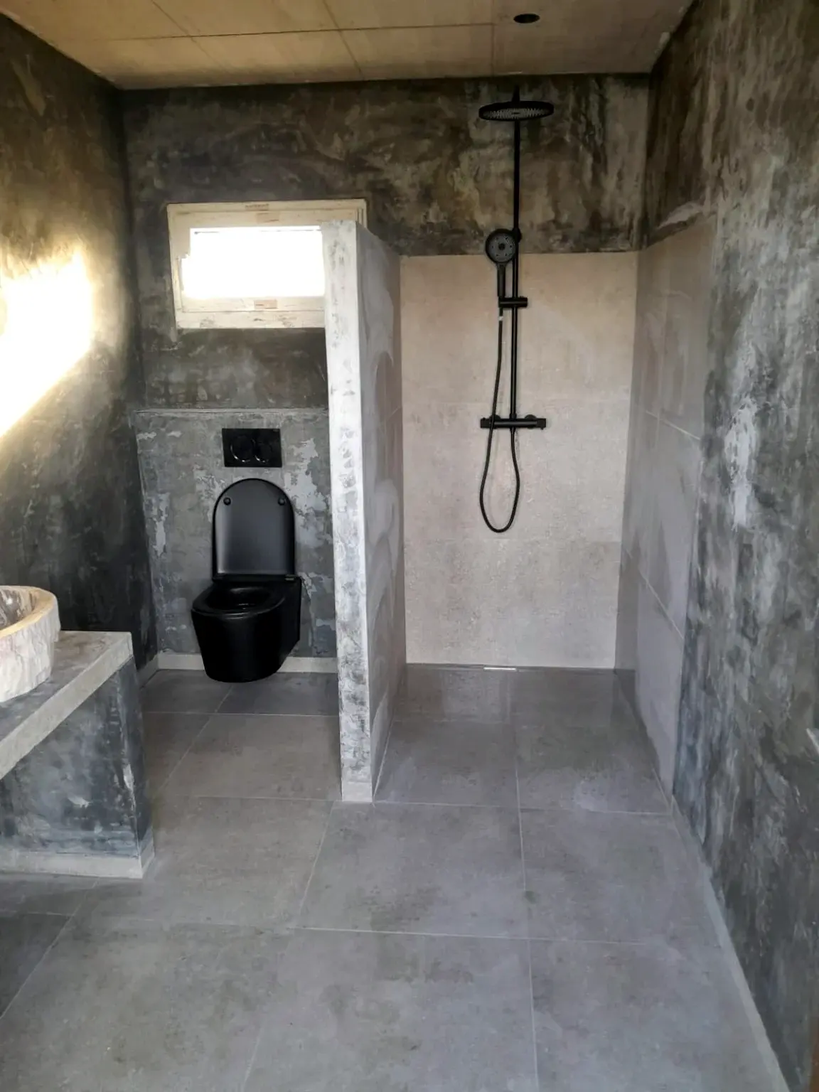 Salle de bains minérale avec douche à l’italienne et sanitaires noirs.
