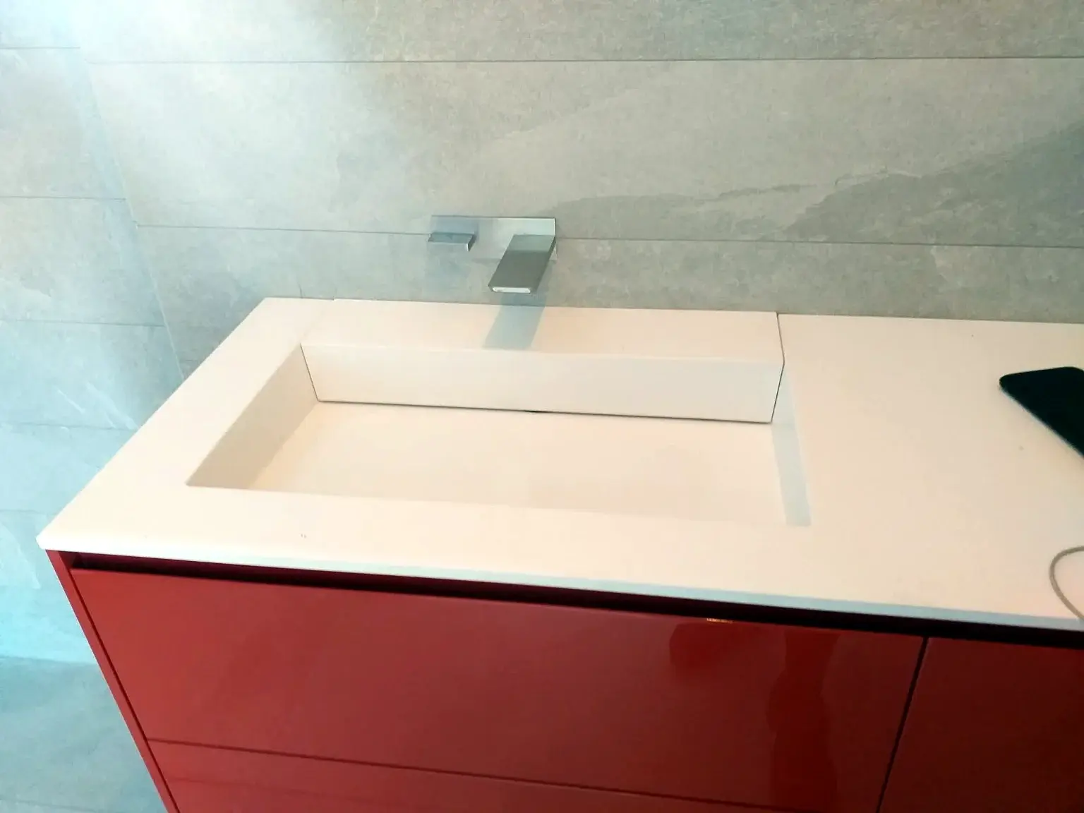 Détail d’une vasque intégrée blanche sur un meuble rouge brillant.