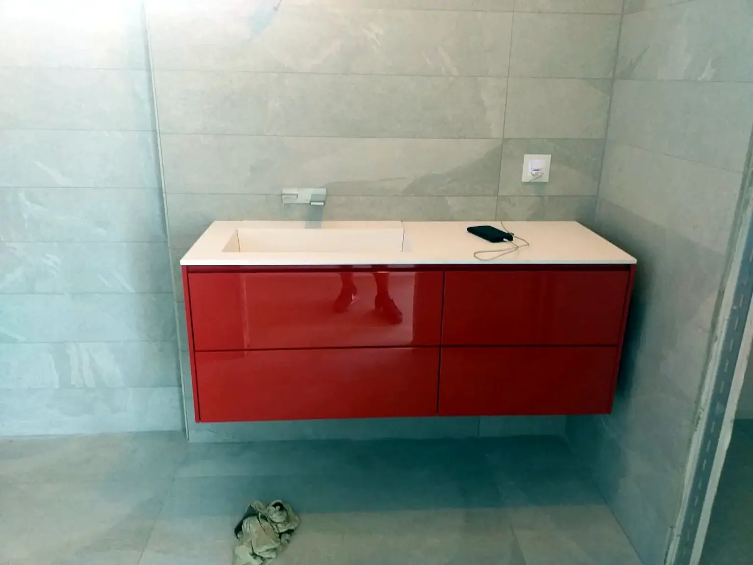 Vue frontale d’un meuble vasque rouge suspendu dans une salle de bains grise.
