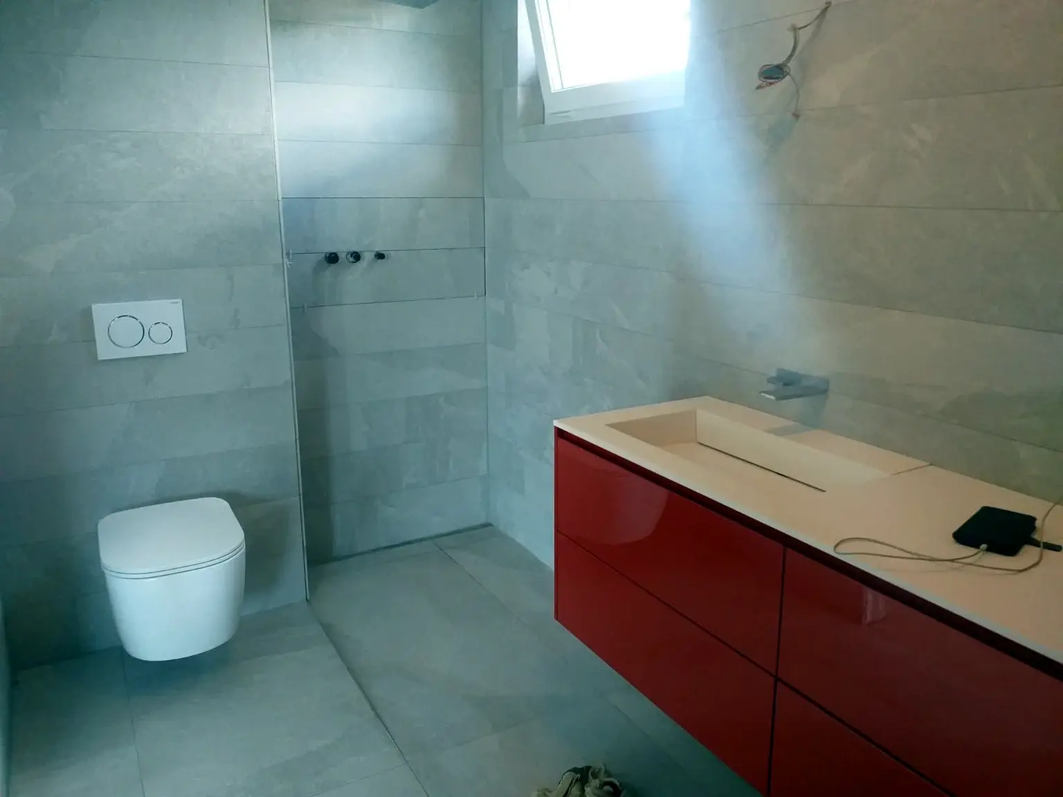 Salle de bains moderne avec meuble vasque rouge, toilettes suspendues et douche ouverte.