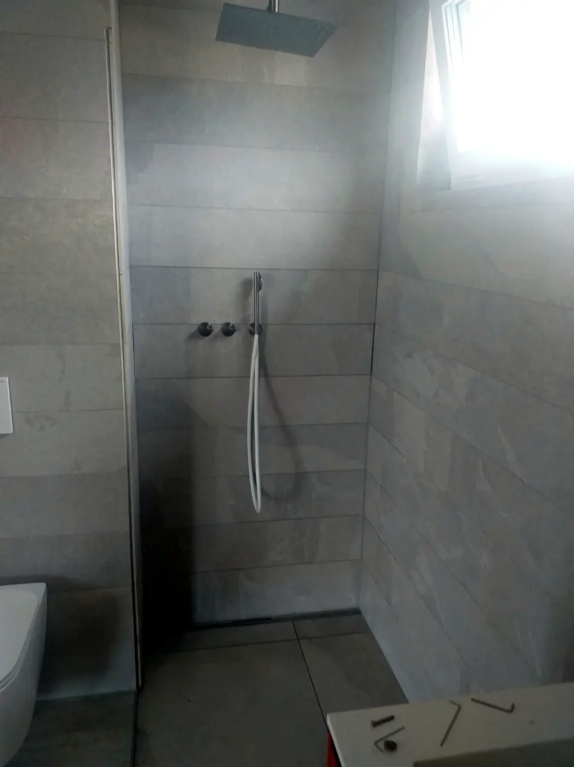 Douche à l’italienne grise avec ciel de pluie et douchette encastrée.