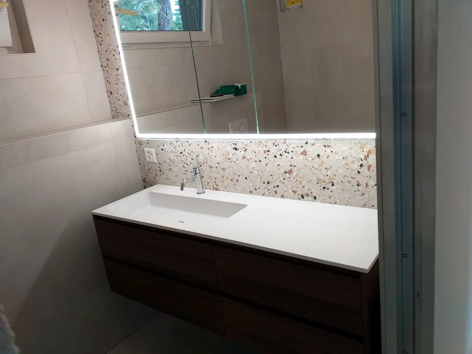 Meuble vasque en bois avec grand miroir lumineux et crédence terrazzo.