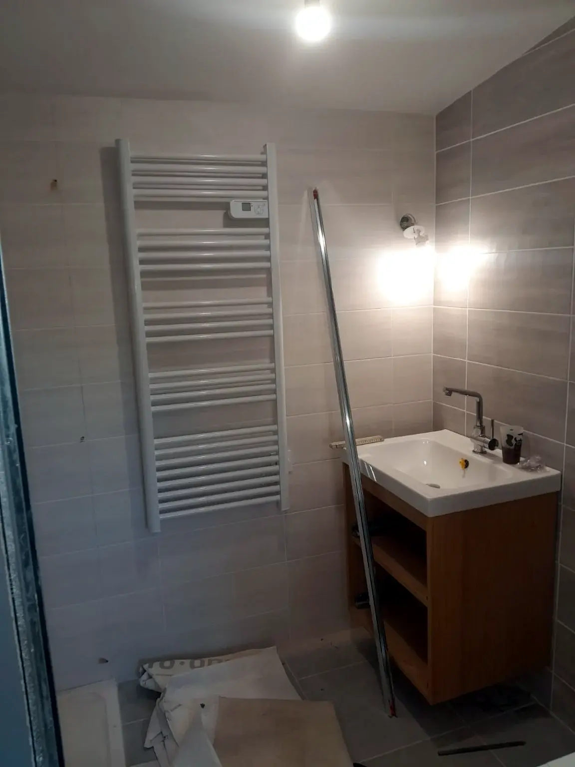Salle de bains en cours d’installation avec meuble vasque en bois et sèche-serviettes.
