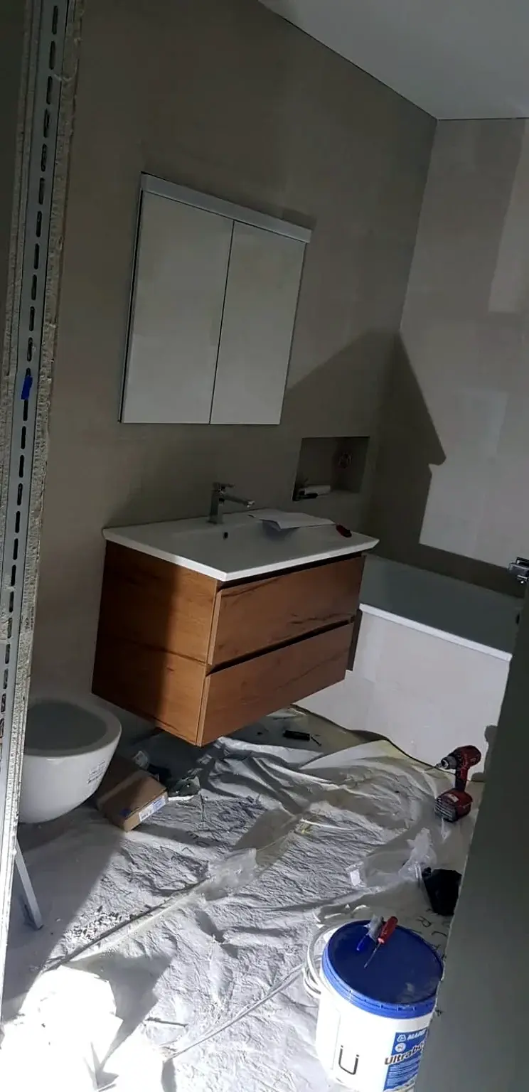 Salle de bains en cours d’installation avec meuble vasque en bois et baignoire.