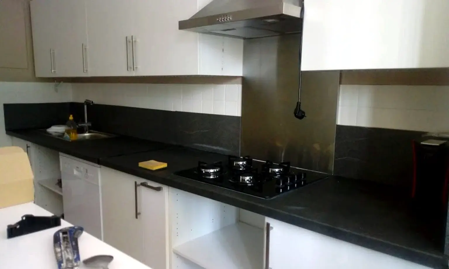 Cuisine blanche avec plan de travail noir, plaque de cuisson et hotte inox.