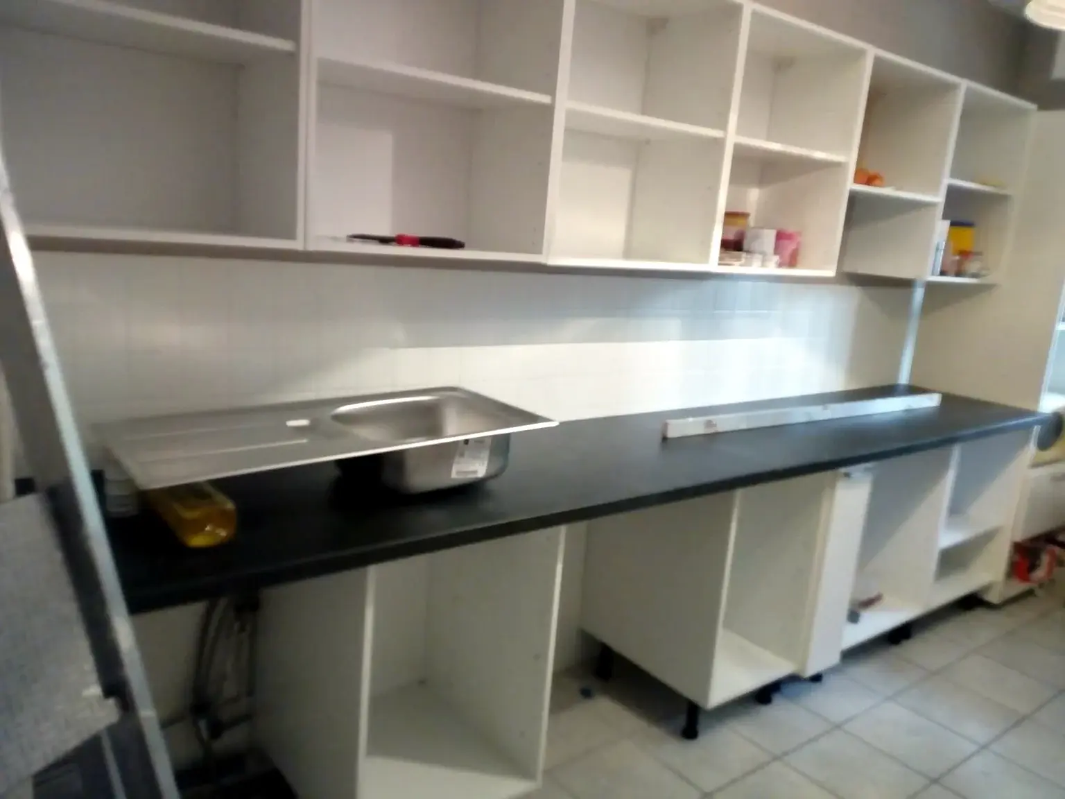 Cuisine blanche en cours de montage avec plan de travail sombre et évier en préparation.