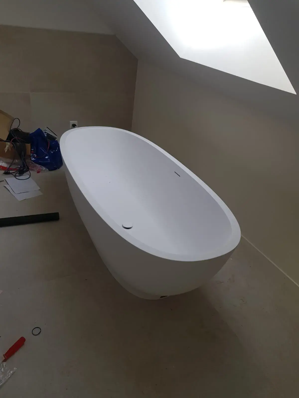Baignoire îlot devant un mur en marbre blanc veiné avec bandeau de mosaïque foncée.