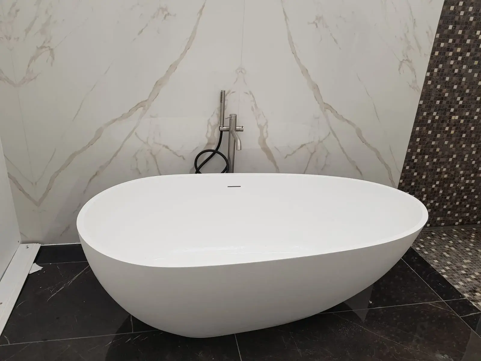 Baignoire îlot vue de face, mitigeur sur pied chromé, mur en marbre blanc et mosaïque.