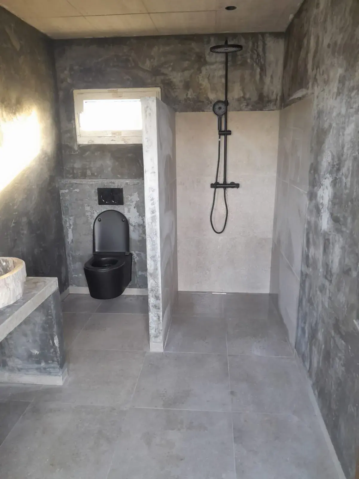 Salle de bain terminée à finition béton brut : douche et WC suspendu noir, robinetterie noire encastrée.