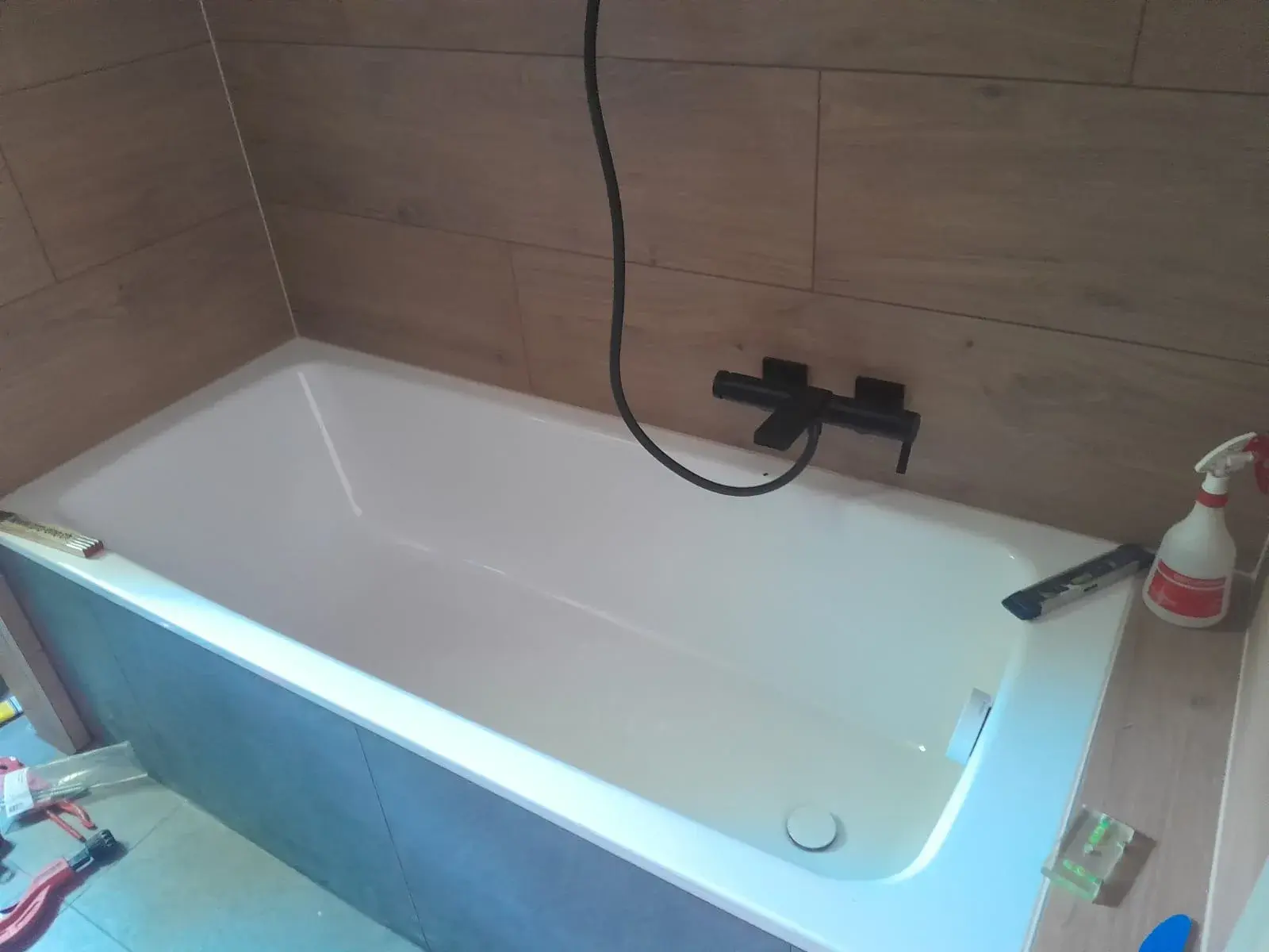 Baignoire encastrée avec mitigeur noir posé, douchette pas encore raccordée.