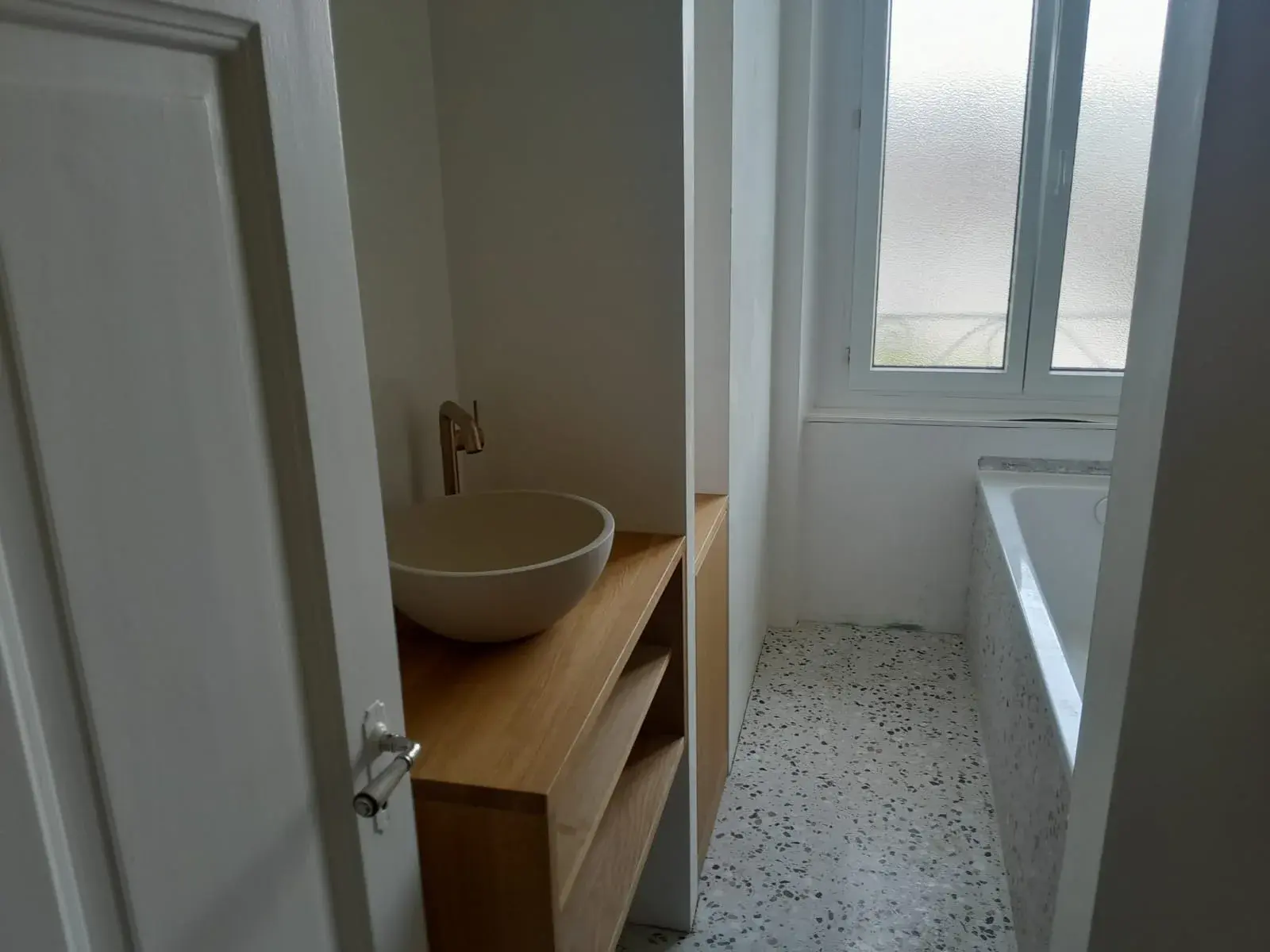 Vasque en pierre et console bois vues depuis le couloir d’accès, sol en terrazzo.