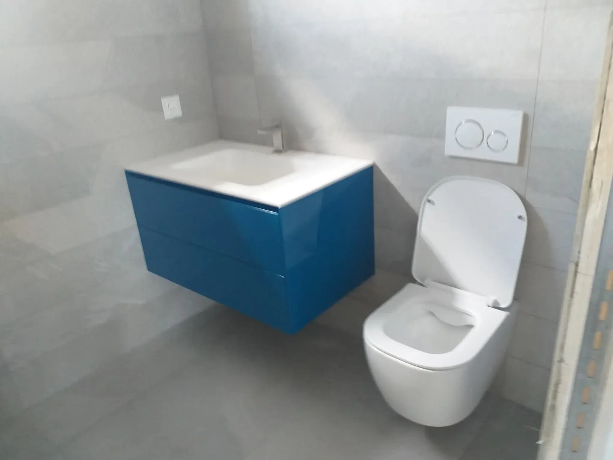 Vue large de la salle de bain bleue avec vasque bleue et WC suspendu blanc.