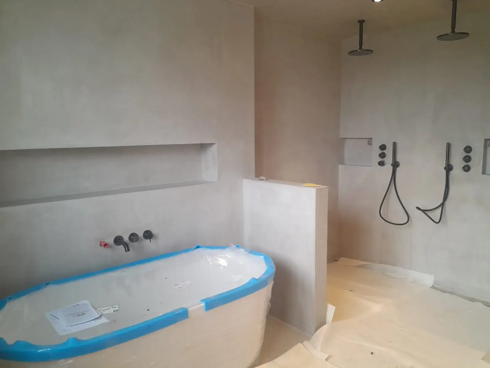 Salle de bain design : baignoire îlot (encore protégée) et deux douches de pluie noires encastrées, finition minérale.