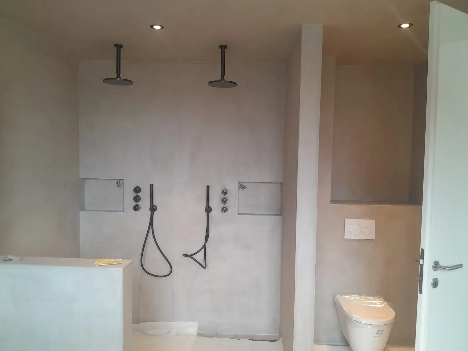 Vue large : WC suspendu et deux douches de pluie noires encastrées, salle de bain design.