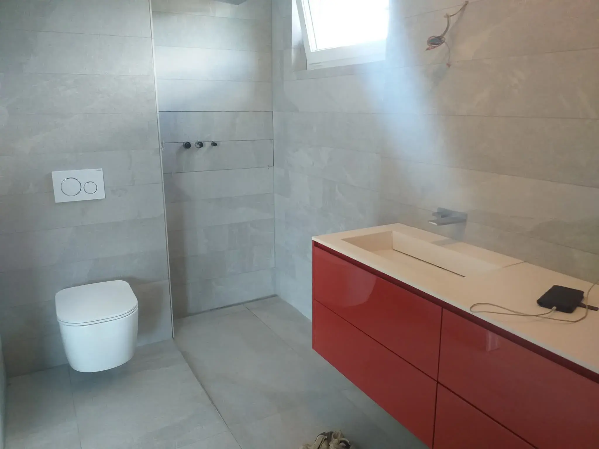 Vue large de la salle de bain rouge : vasque rouge, WC suspendu blanc et douche à l’italienne.