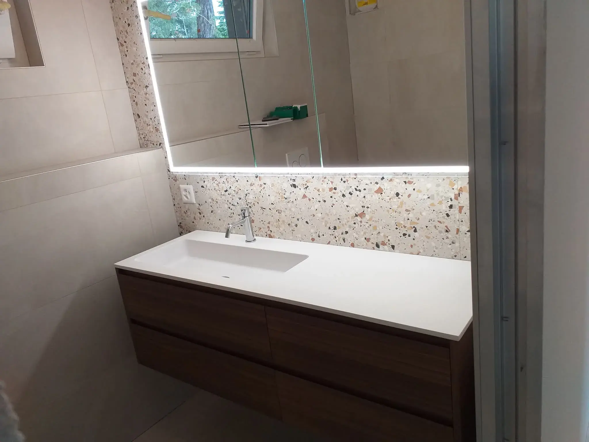 Vasque en bois sombre avec crédence terrazzo et miroir rétroéclairé.