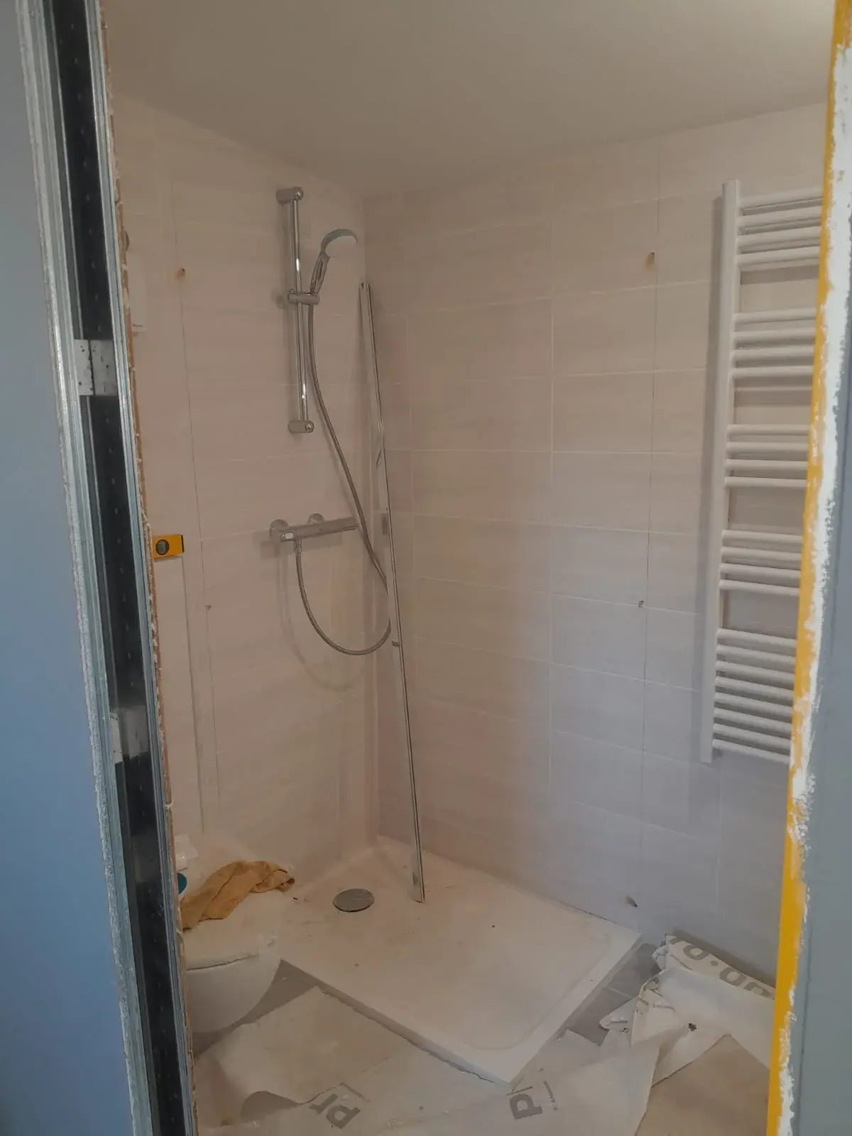 Vue d’ensemble : douche à paroi vitrée et WC suspendu, salle de bain en finition.