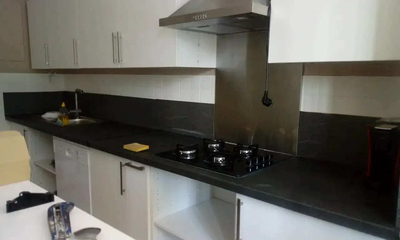 Cuisine moderne finie : façades avec poignées posées, plaque de cuisson, hotte et lave-vaisselle intégrés.