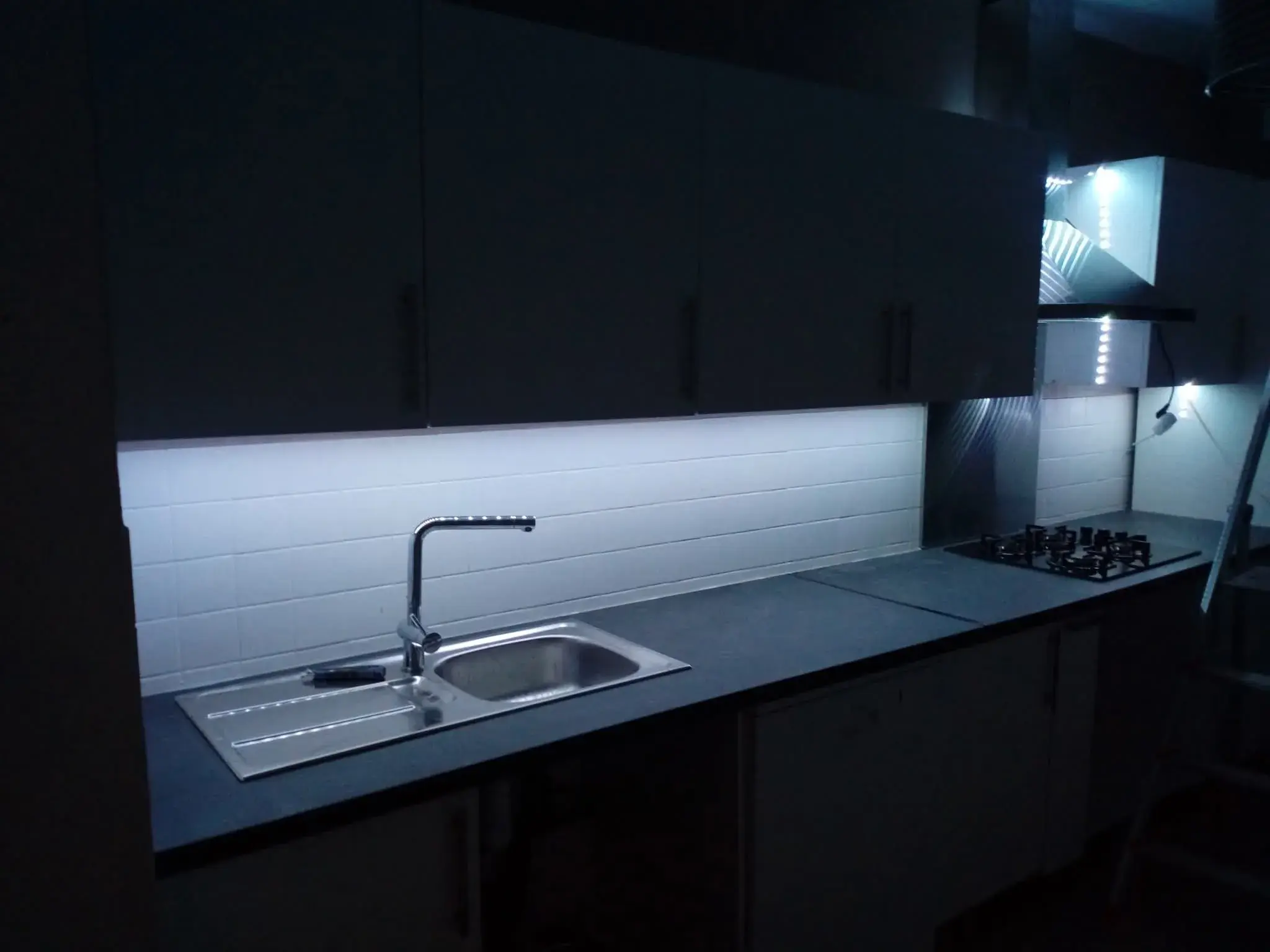 Cuisine moderne de nuit, plan de travail éclairé par un bandeau LED sous les caissons hauts.