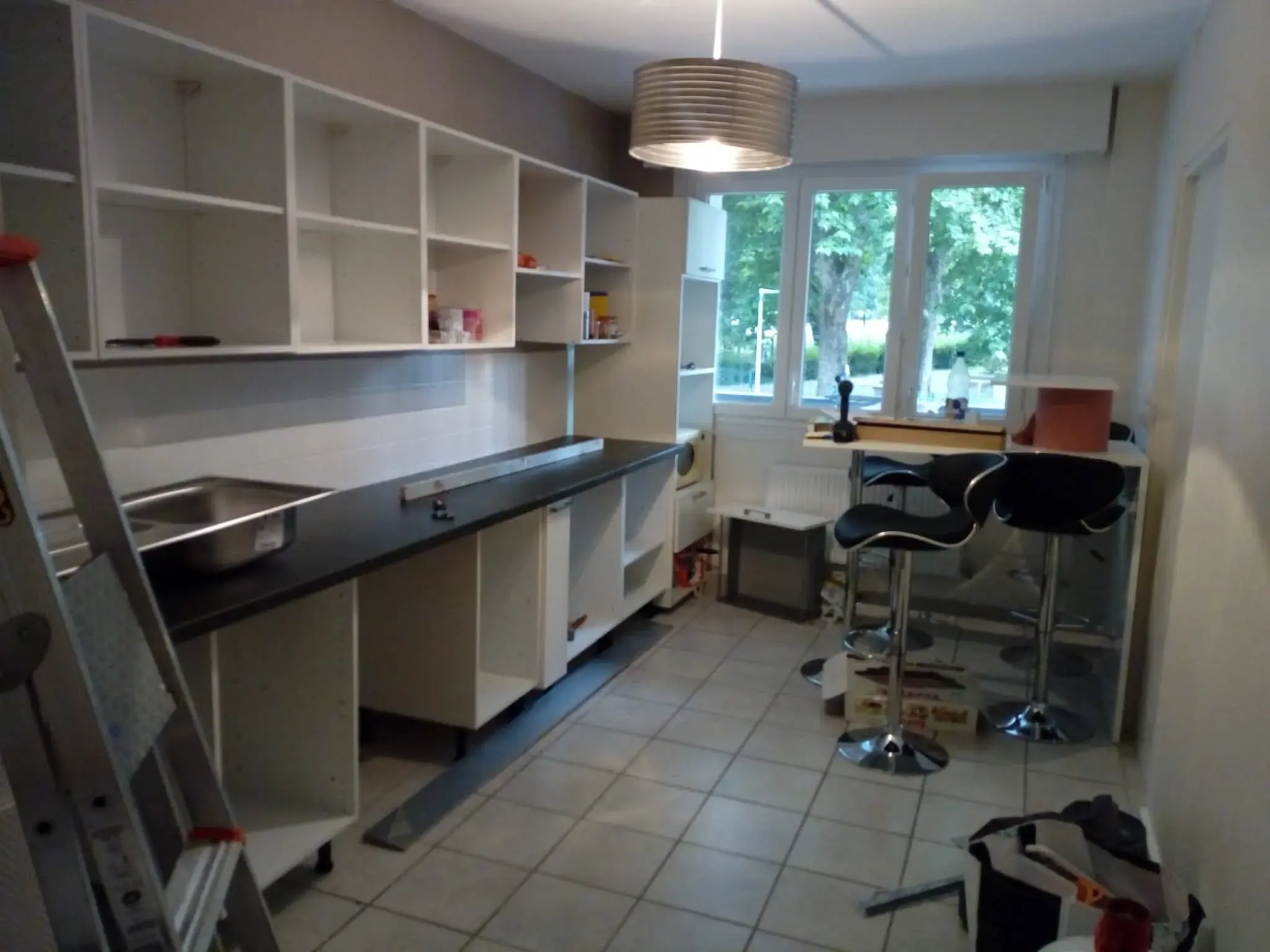 Vue large de la cuisine moderne en pose avec coin dînatoire (tabourets hauts) et suspension.